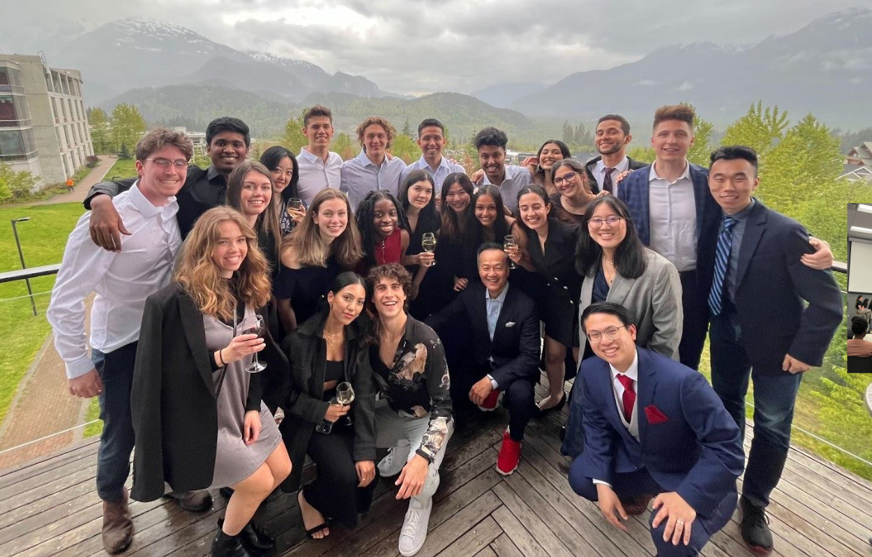 A group of students stand in rows outside, smiling at the camera
